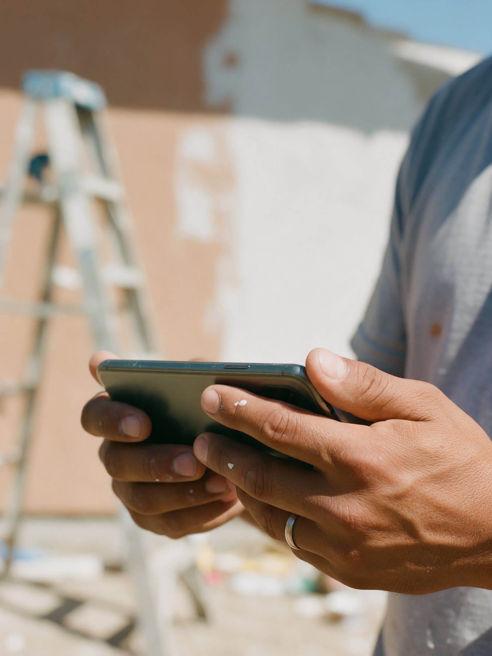 A worker's hands, with paint on the fingers, hold a phone on the job site.