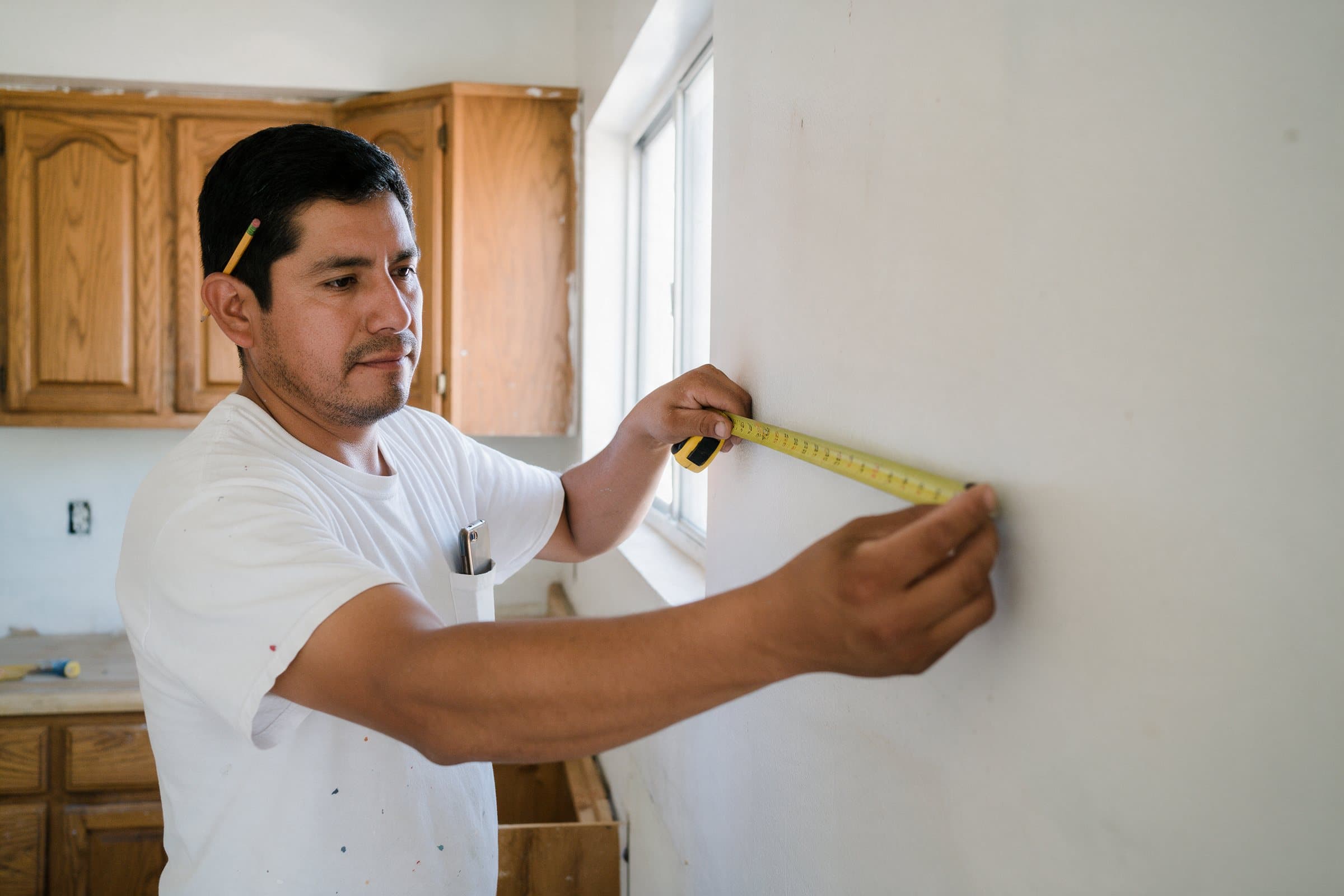 A contractor measures a kitchen wall with his tape measure.